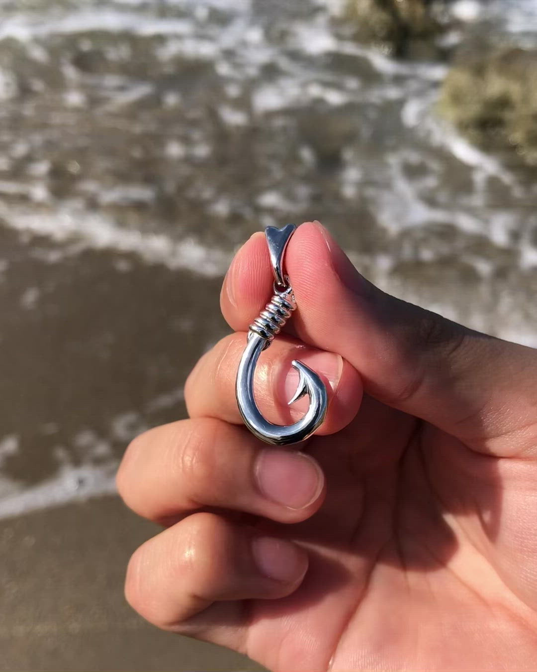 Video highlighting the details of a silver hook pendant, in a live beach setting.